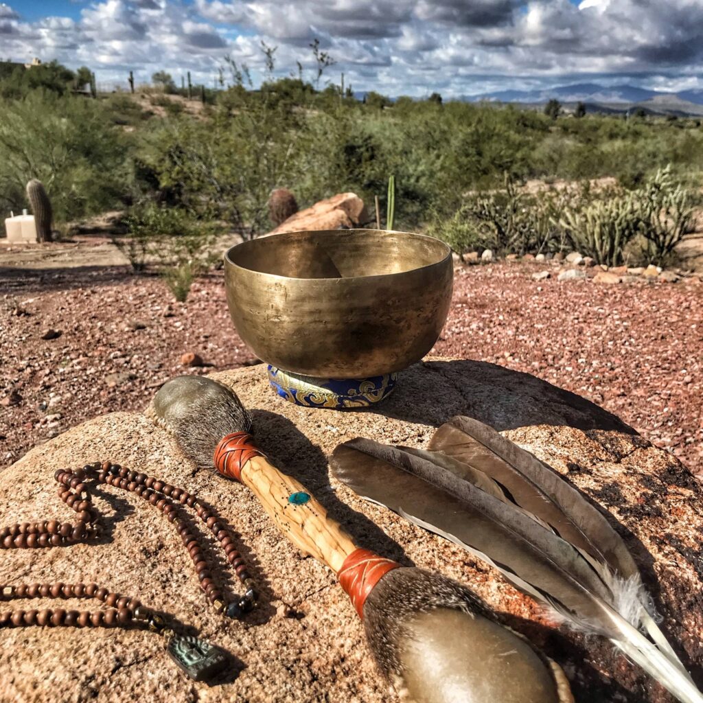 A cloth laid on the ground with a staff, a rattle, feathers and small stones arranged across it.
