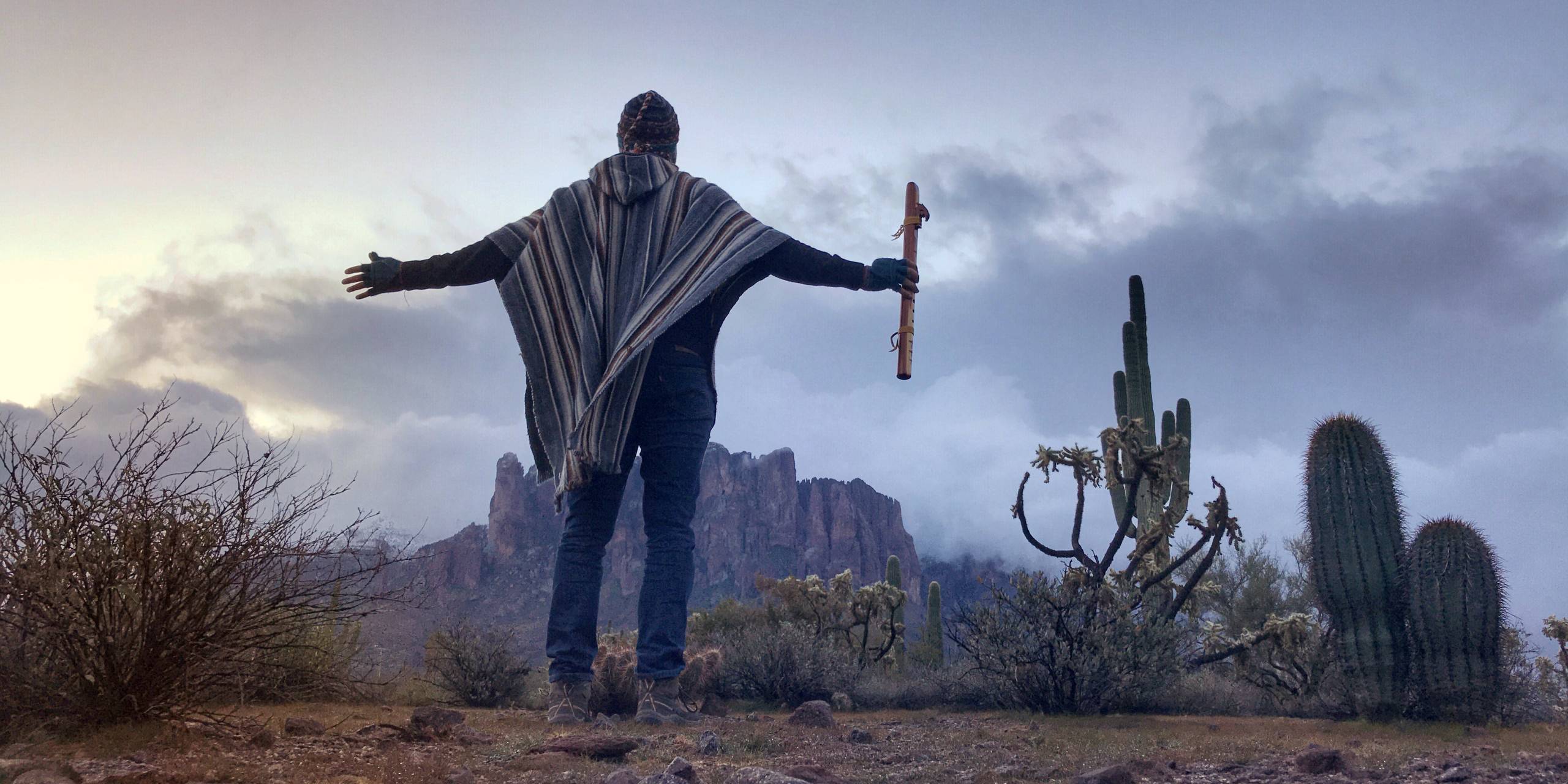 A person standing with both
  arms open toward a range of mountains.