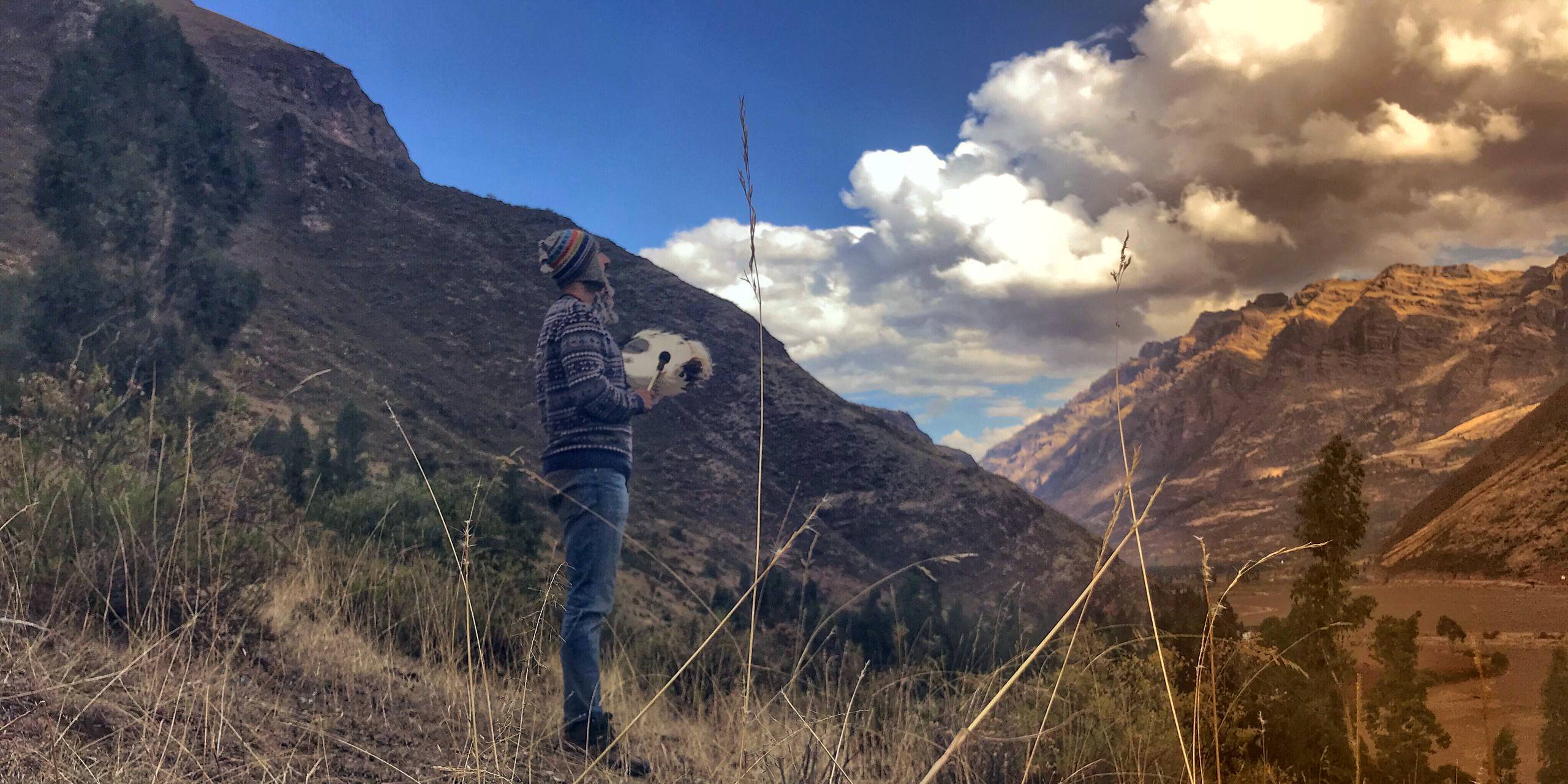 A person holding a frame drum above
a wide valley, ridges receding behind them.