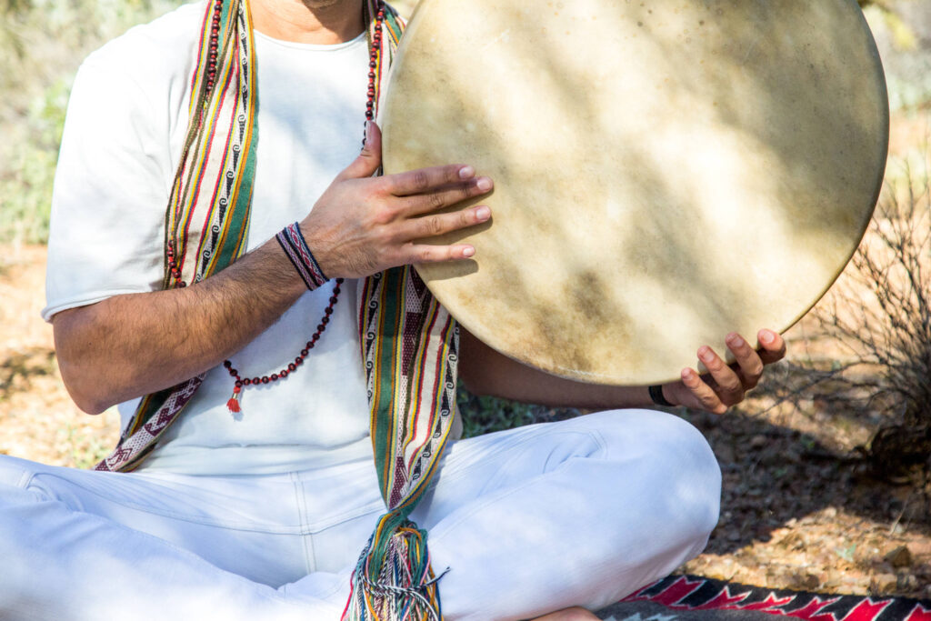 Two hands resting on the skin of a
  frame drum, the beater held between them.