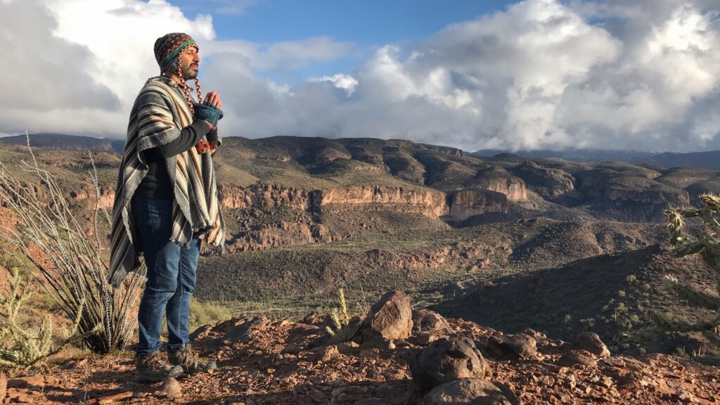 A figure standing at the rim
  of a canyon with both hands raised, the far wall in shadow behind them.